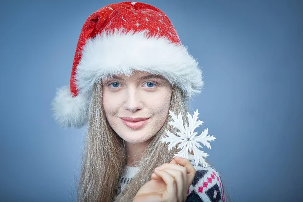 Menina congelada com neve no rosto usando chapéu de Santa segurando floco de neve — Fotografia de Stock