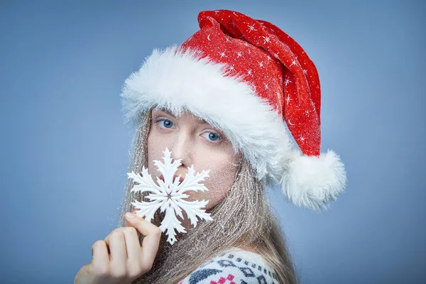 Frozen girl with snow on face wearing Santa hat holding snowflake — Stock Photo, Image