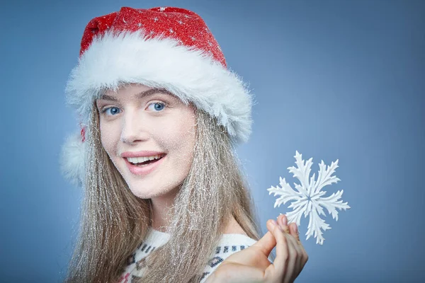 Menina congelada com neve no rosto usando chapéu de Santa segurando floco de neve — Fotografia de Stock