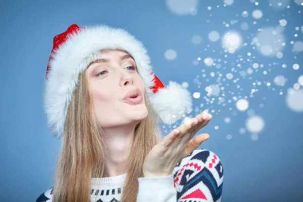 Femme portant le chapeau de Père Noël soufflant à la paume ouverte avec de la neige — Photo