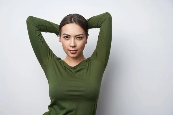 Smiling brunette female in green shirt standing with hands over head — Stock Fotó