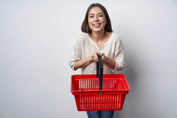 Ler brunett kvinna som står vid vita väggen håller tom varukorg — Stockfoto