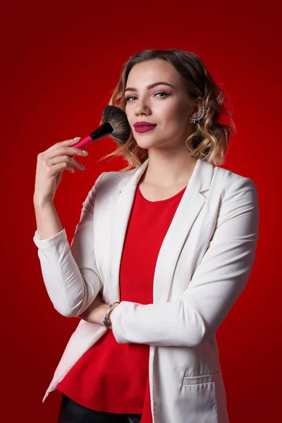 Vrouwelijke stylist permanent met make-up borstel op rode achtergrond — Stockfoto