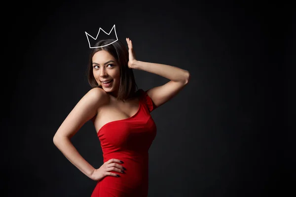 Schöne Frau im roten Kleid, die ihre Krone stützt — Stockfoto