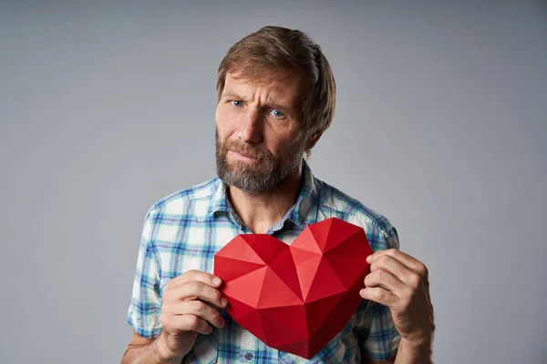 Homme mûr malheureux en chemise à carreaux tenant la forme du cœur — Photo