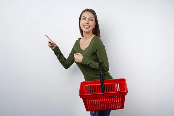 Woman holding empty shopping basket pointing to side — Stock Photo, Image