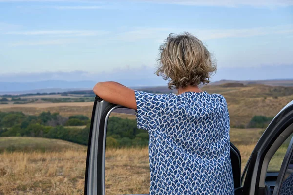 Woman standing leaning on a car door — Stock Photo, Image