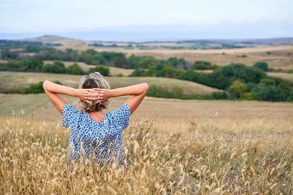 Vue arrière d'une femme assise dans de l'herbe sèche stérile, regardant à l'horizon — Photo