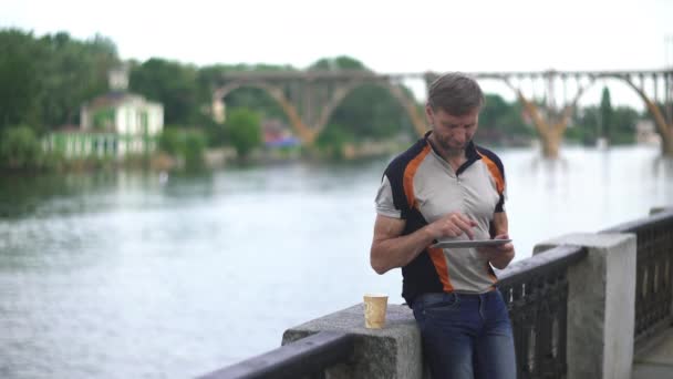 Зрелый человек просматривает цифровые планшеты летом, на набережной реки — стоковое видео