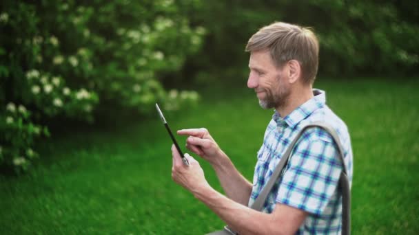 Mature man browsing on digital tablet on green nature background — Stock Video
