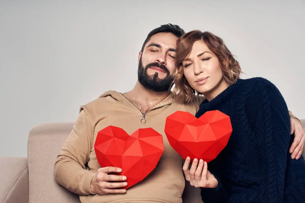 Усміхнена пара сидить на дивані, тримаючи форму серця — стокове фото