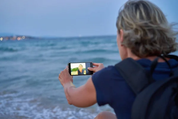 Mujer tomando un autorretrato en el teléfono inteligente de la playa en la puesta del sol en — Foto de Stock