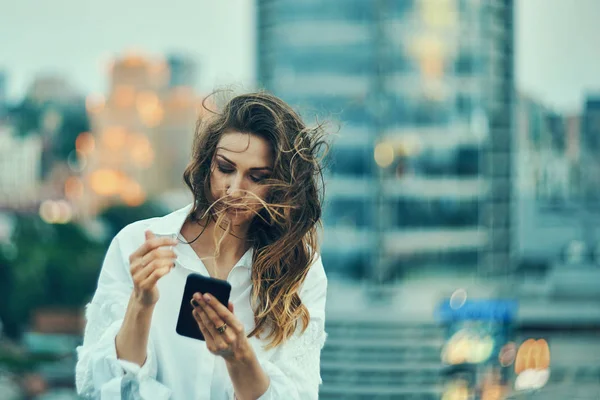 Молодая женщина над городским пейзажем держит смс-ку со смартфона — стоковое фото