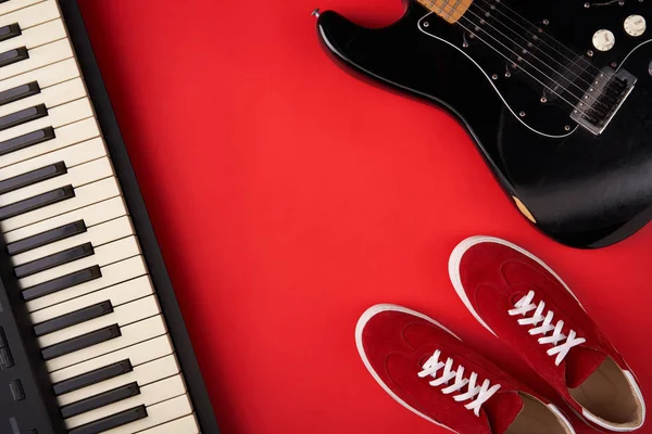 Elektrische gitaar, synthesizer en rode stijlvolle sneakers, op rode achtergrond — Stockfoto