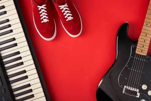 Chitarra elettrica, sintetizzatore e scarpe da ginnastica rosse alla moda, su sfondo rosso — Foto Stock