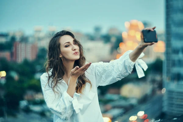 Mujer haciendo autorretrato con su teléfono inteligente sobre la puesta de sol de oro paisaje urbano — Foto de Stock