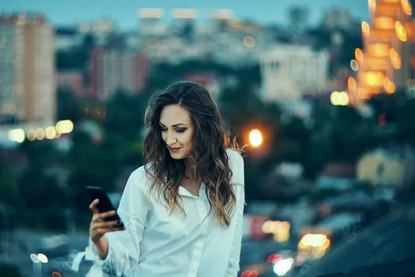 Mujer joven sobre paisaje urbano sosteniendo un teléfono inteligente mensajes de texto — Foto de Stock