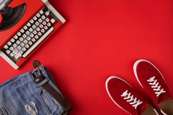 Röd mocka sneakers skor, nödställda jeans och skrivmaskin på röd bakgrund — Stockfoto