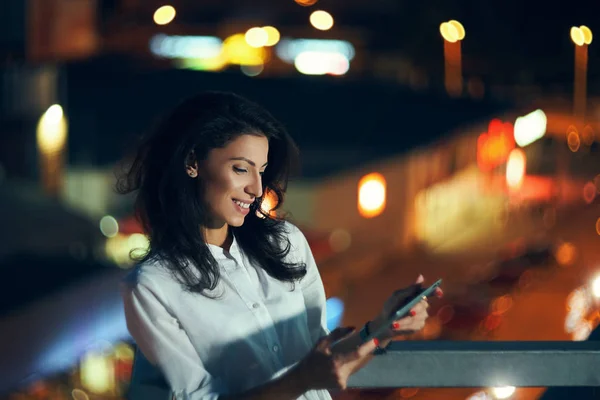 Γυναίκα πάνω από το νυχτερινό αστικό τοπίο κρατώντας ένα ψηφιακό μήνυμα tablet — Φωτογραφία Αρχείου