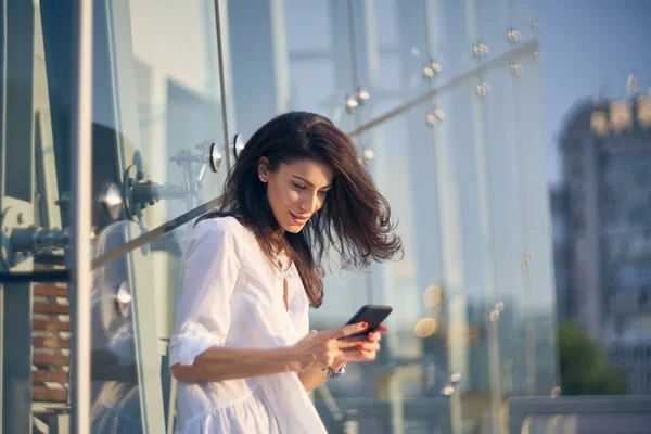 Mujer joven sobre paisaje urbano sosteniendo un teléfono inteligente mensajes de texto — Foto de Stock