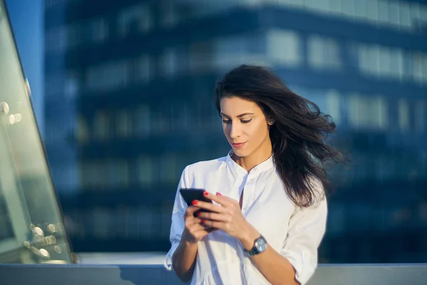Νεαρή γυναίκα πάνω από το αστικό τοπίο κρατώντας ένα έξυπνο τηλέφωνο μηνύματα — Φωτογραφία Αρχείου