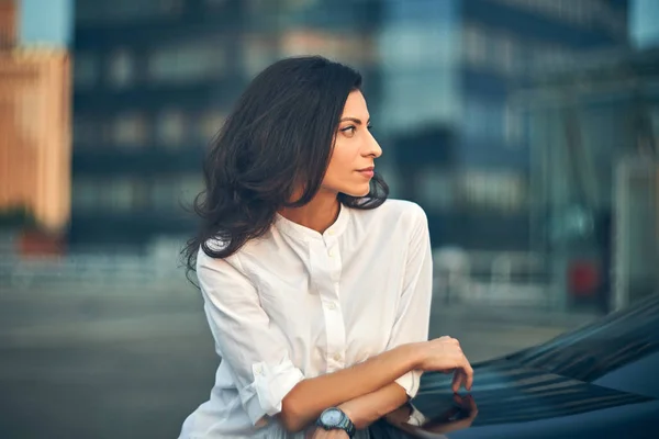 Fiatal nő támaszkodva egy autó a modern irodai homlokzat — Stock Fotó