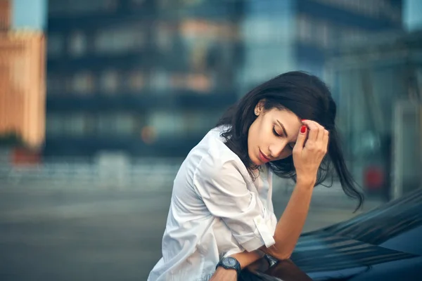 Junge Frau lehnt an Auto über moderne Bürofassade — Stockfoto