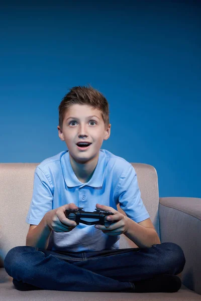 Koncepcja gier. Chłopiec siedzi na kanapie grając w gry wideo z joystickiem — Zdjęcie stockowe