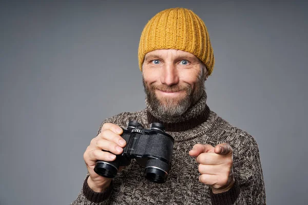 Hombre maduro sonriente en suéter cálido y sombrero de punto con prismáticos — Foto de Stock