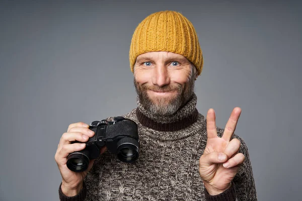 Hombre maduro en suéter cálido y sombrero de punto con prismáticos gestos OK — Foto de Stock