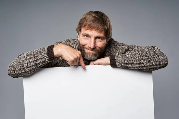 Улыбающийся взрослый мужчина в тёплом свитере, опирающийся на белый баннер — стоковое фото