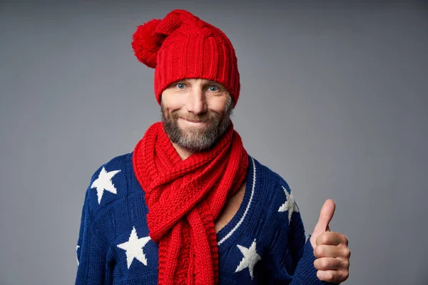 Sonriente hombre maduro con sombrero de punto rojo brillante y bufanda gesto pulgar hacia arriba —  Fotos de Stock