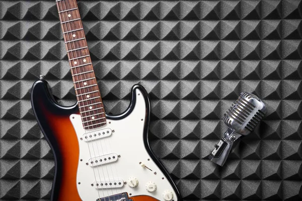 Guitarra elétrica e microfone retro no painel de espuma acústica — Fotografia de Stock