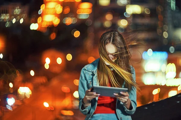 Девушка на ночном фоне городской пейзаж с уличным освещением, используя цифровой планшет — стоковое фото