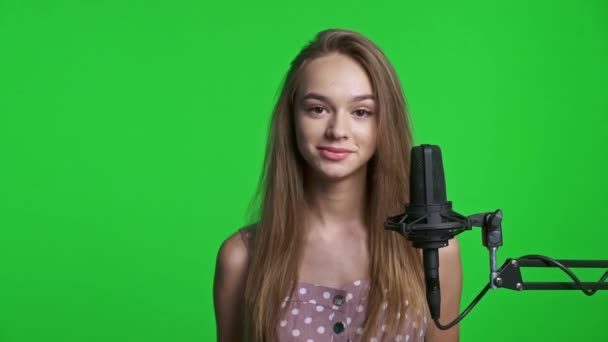 미소짓는 소녀가 마이크로폰 이야기하고 엄지손가락을 흔들면서 카메라 크로마 배경을 — 비디오