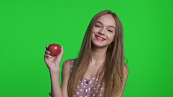 Uśmiechnięta dziewczyna w letniej sukience uśmiechnięta i trzymająca czerwone jabłko — Wideo stockowe