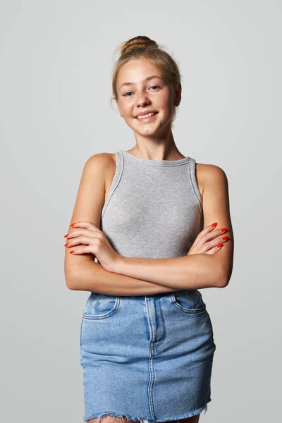 Teen girl in denim skirt looking at camera smiling, studio portrait