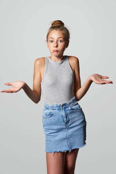 Teen girl in denim skirt looking at camera shrugging her shoulders and pouting lips, studio portrait
