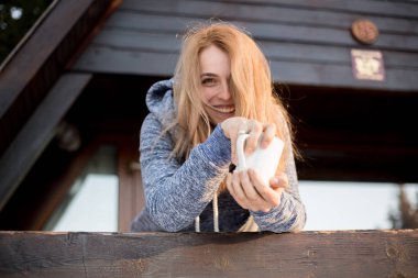 Beyaz Kupası ahşap evin terasında ayakta ve gülümseyen güzel kadın 