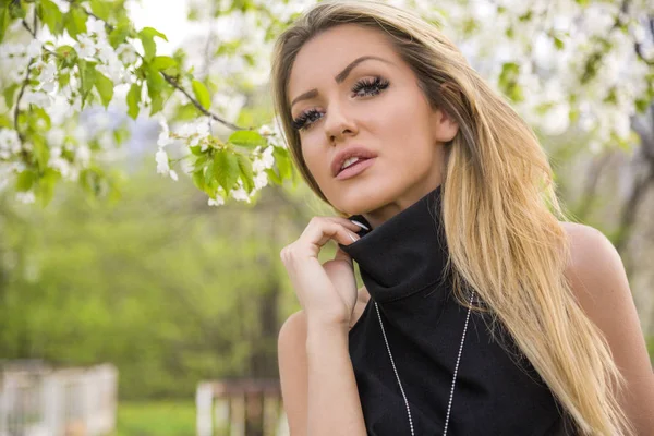 Beautiful woman with blonde hair in black dress posing on camera in park