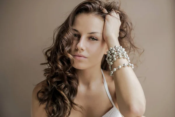 beautiful brown-haired woman touching hair and looking at camera at home