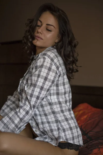 市松模様のシャツと下着を自宅のベッドの上に座って美しい茶色の髪の少女 — ストック写真
