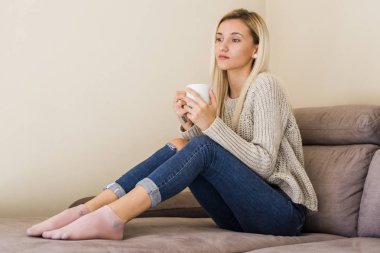 kot pantolon ve kazak fincan kahve ile kanepede rahatlatıcı çekici genç kadın