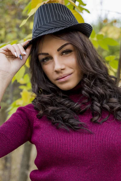 portrait of beautiful young woman in sweater and hat in autumnal park