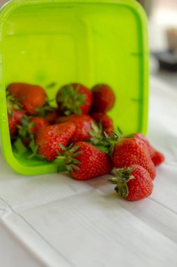 beyaz masa örtüsü üzerinde yeşil konteyner düşen taze çilek