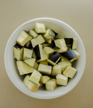 Cubes of eggplant on bowl on wooden table clipart