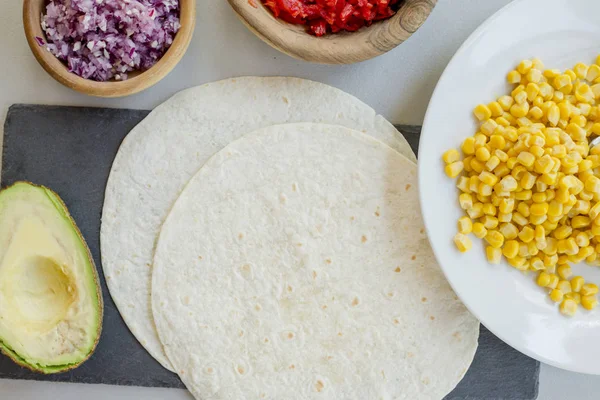 ingredients for Mexican vegetarian tacos in bowls on light table, close-up