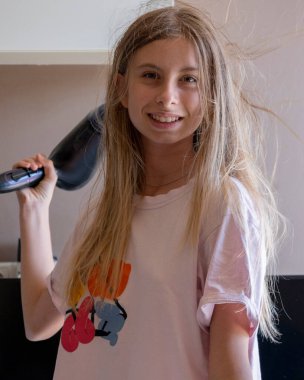 Mutlu 12 yaşındaki kız evde saçlarını kurutuyor dans ediyor ve gülümsüyor.