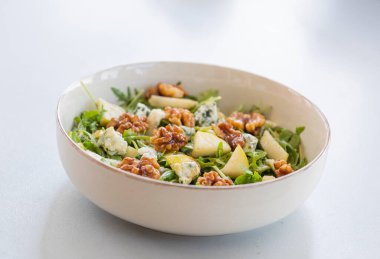 Taze sonbahar salatası, roka, olgun armut dilimleri ve çıtır çıtır ceviz, canlı renklerde sağlıklı sonbahar öğle yemeği fikri.