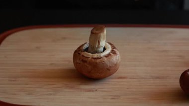 Tahta kesme tahtasına yerleştirilmiş taze şampiyon mantarlarının yakın çekim videosu.